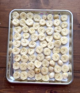Sliced bananas laid out in a single layer on a parchment lined baking sheet.