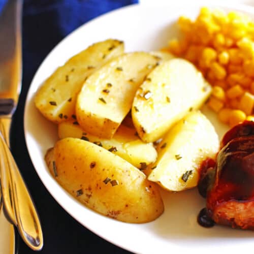 A plate with roasted potato wedges, corn, and bbq chicken.