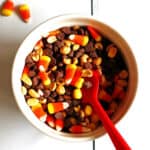 A bowl of candy corn party mix with a red spoon.