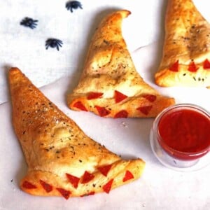 Three Witch Hat Calzones with a small bowl of marinara sauce and some plastic spiders.