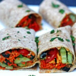 Four whole wheat veggie wraps with tomatoes, hummus, carrots, cilantro, olives, and cucumber.