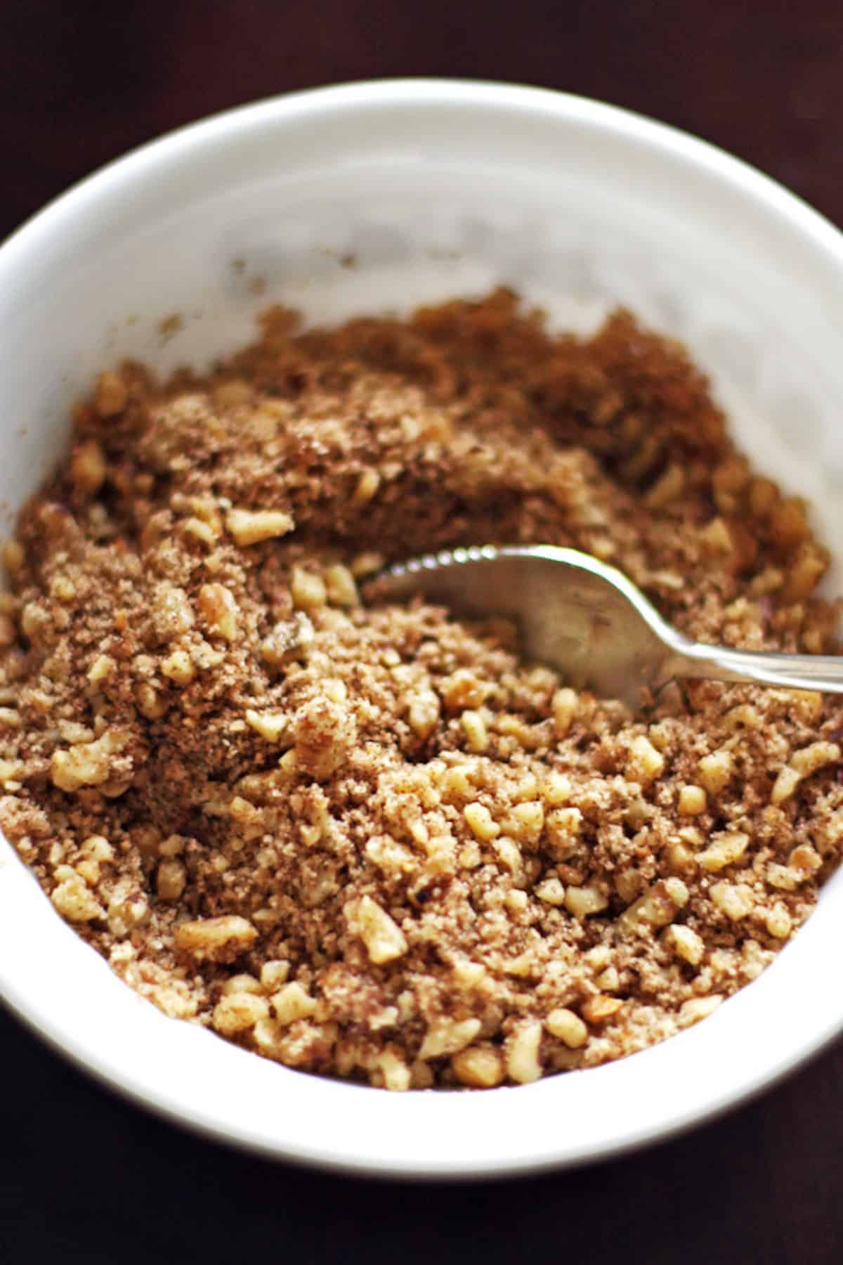 A small bowl of streusel crumble made with brown sugar, walnuts, and flour.