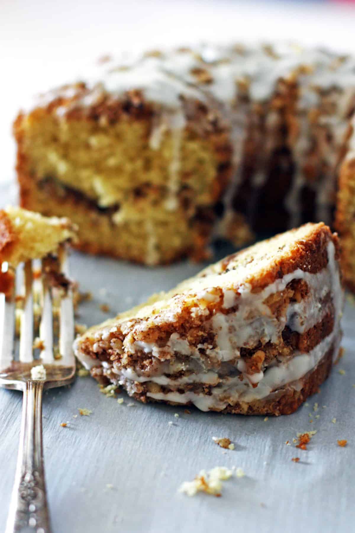 A slice of cinnamon sour cream coffee cake in front of the rest of the cake.