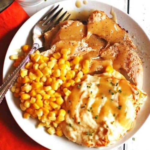 A plate of juicy slow cooker turkey breast smothered in gravy with mashed potatoes and corn.