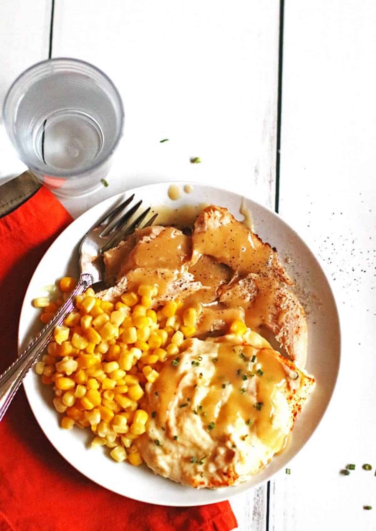 A plate of juicy slow cooker turkey breast smothered in gravy with mashed potatoes and corn.