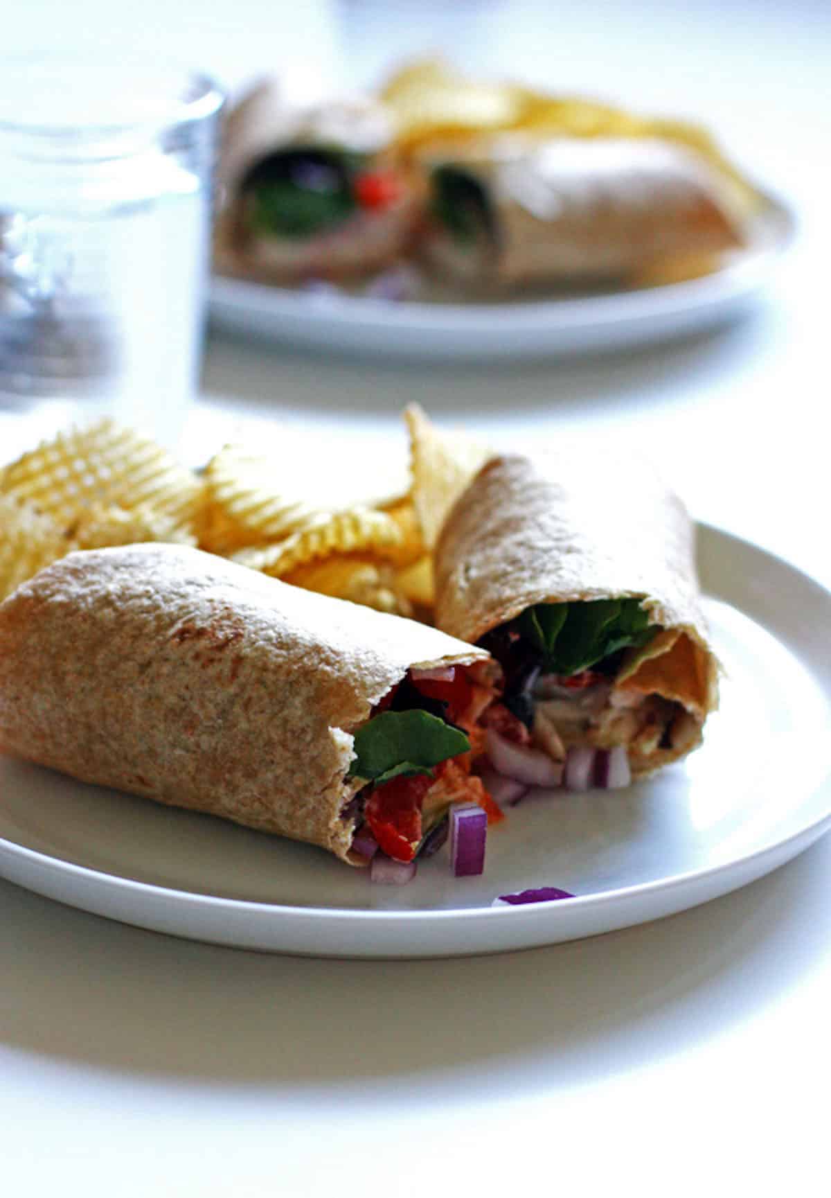 A chicken wrap with cherry tomatoes, cheese, and onions on a plate.