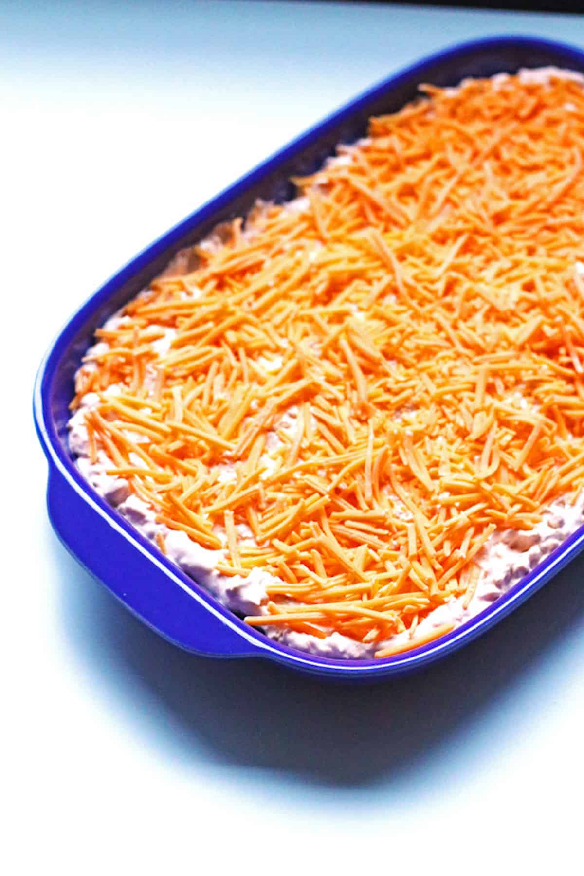 A tray of buffalo chicken dip topped with cheese that hasn't been baked yet.
