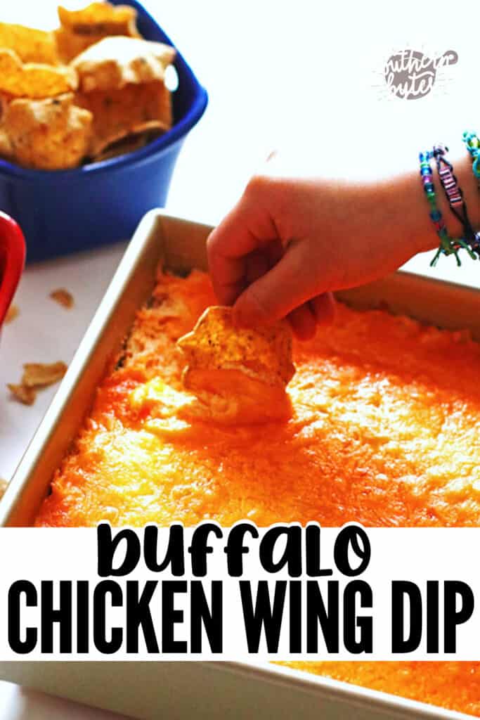 A pin image of a hand scooping up creamy buffalo chicken dip with a corn chip.