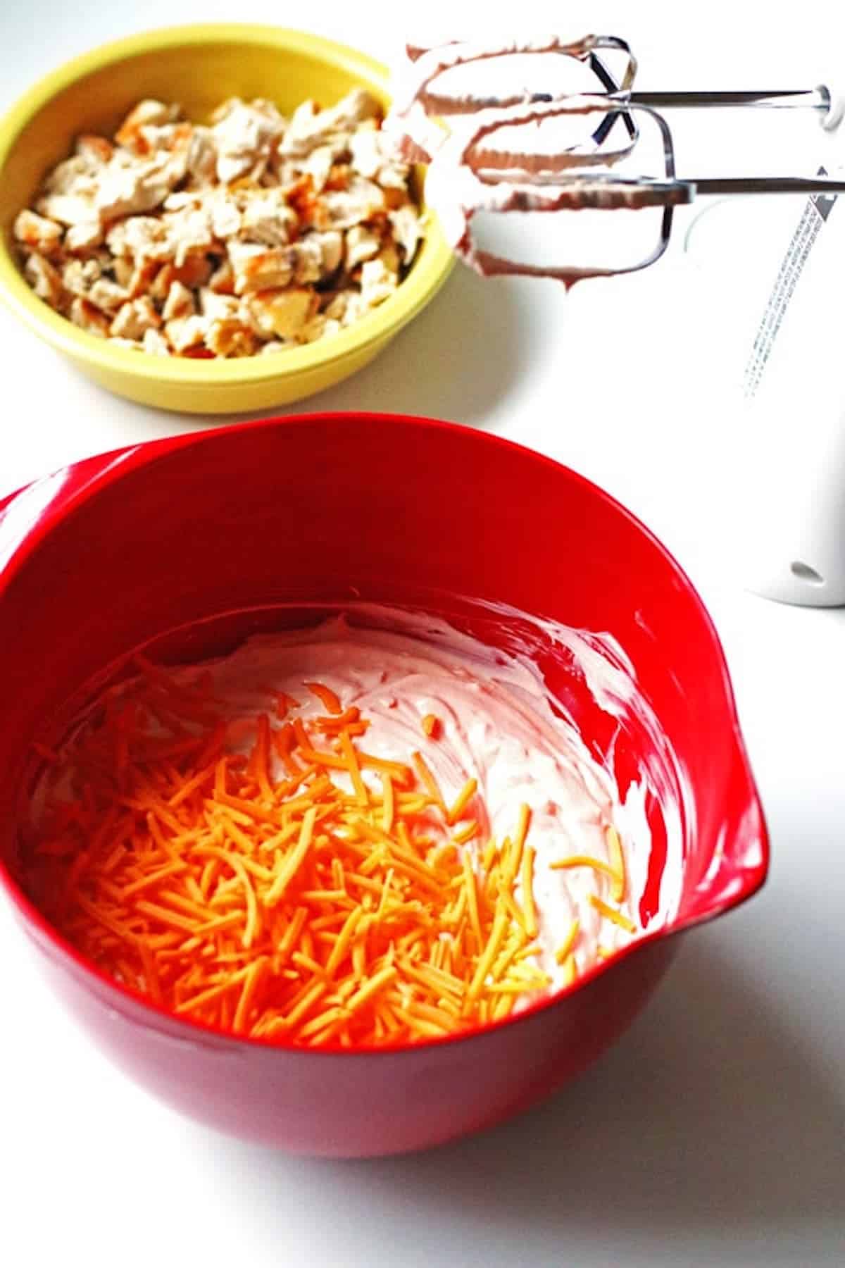 A red bowl with cheese to mix up buffalo chicken dip.