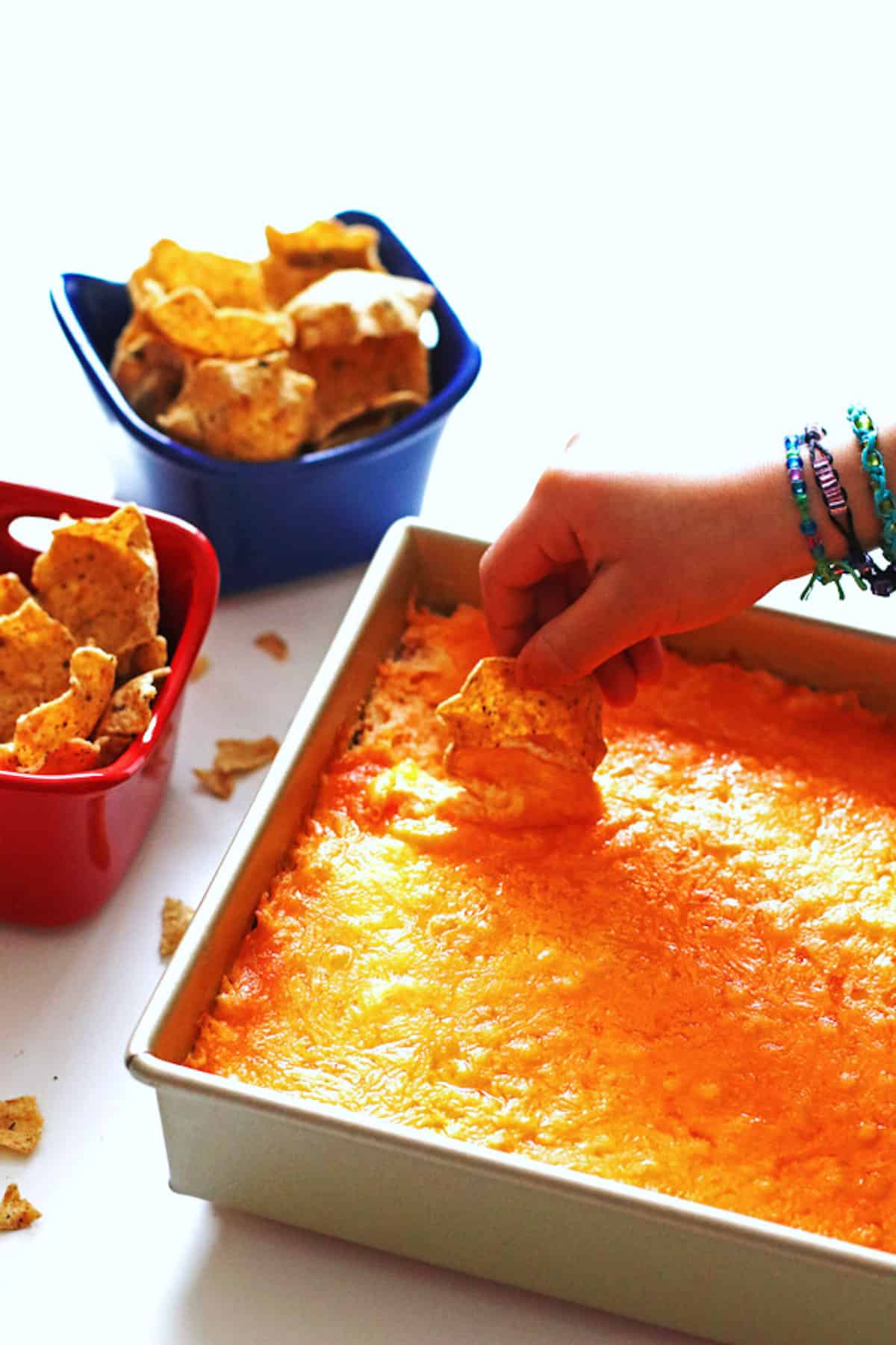 A hand scooping buffalo chicken dip with a corn chip.