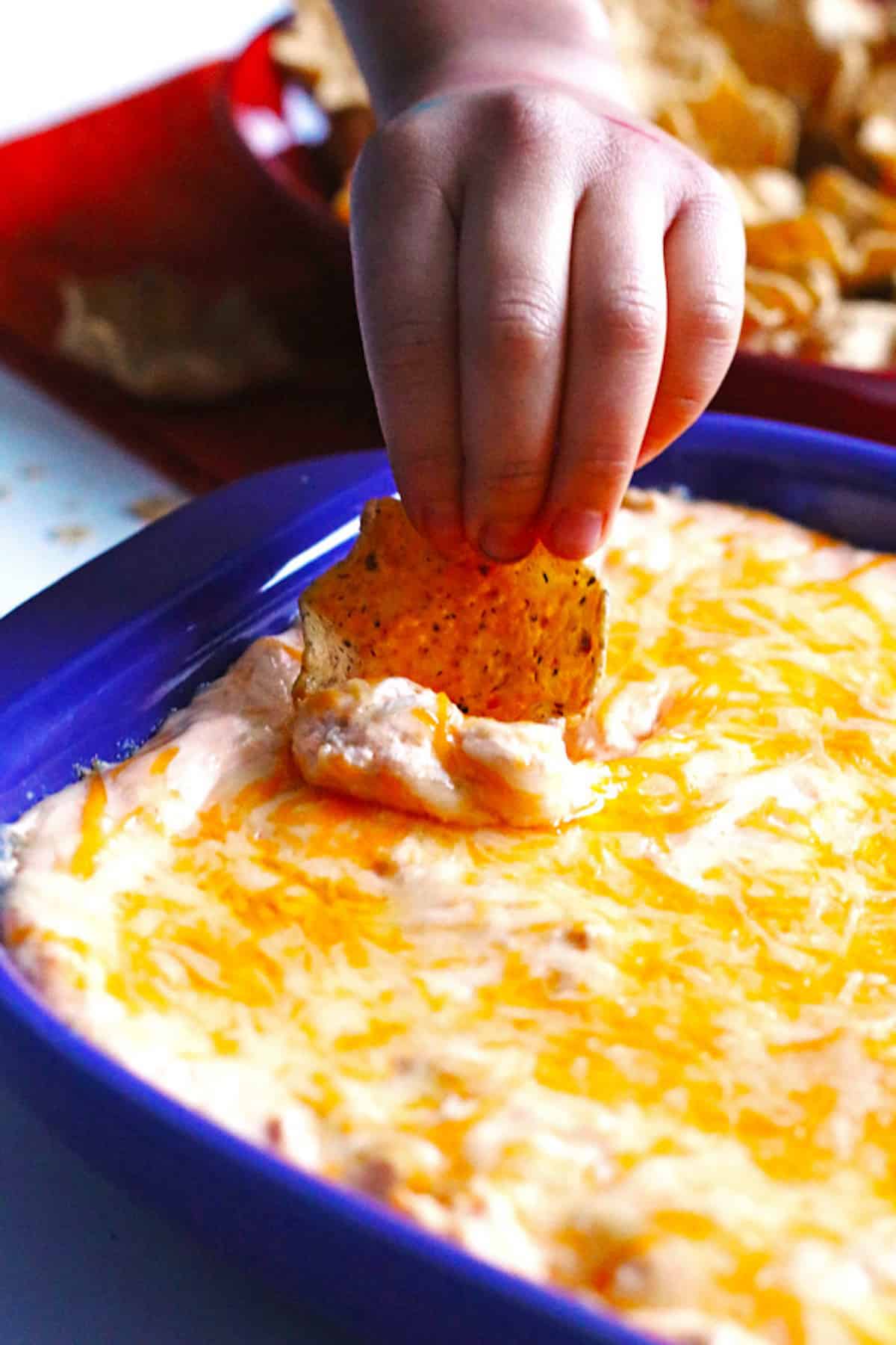 A child's hand scooping buffalo chicken dip with a tortilla chip.