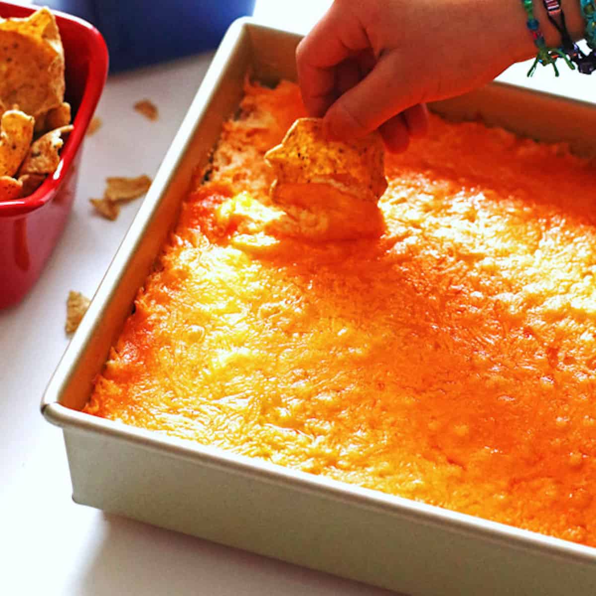 A hand scooping buffalo chicken wing dip with a corn chip.