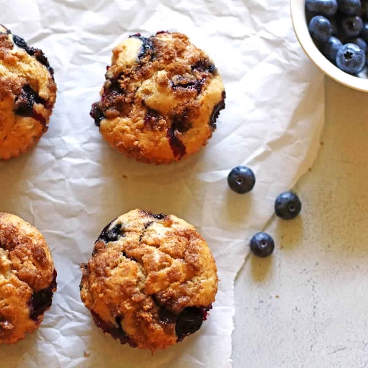 Blueberry Banana Muffins on white parchment paper with a small bowl of blueberries next to them.