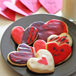 A plate of frosted heart cookies with cards and a glass of milk.