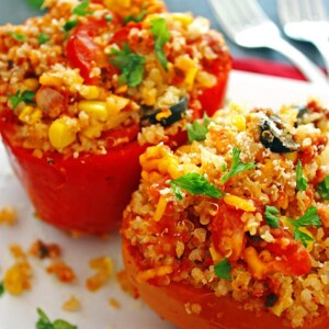 Two red bell peppers stuffed with quinoa and veggies on a white plate.