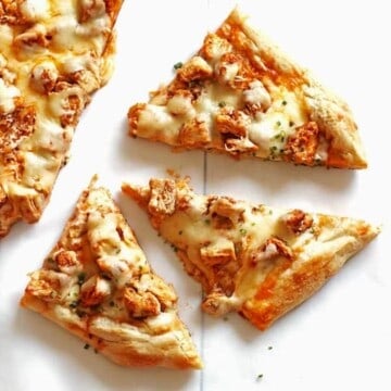Slices of buffalo chicken pizza topped with chives on a white table.