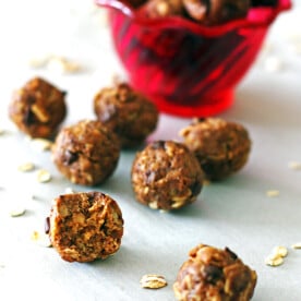 Peanut butter energy balls in front of a red bowl with a bite taken out of one of them.