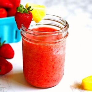Strawberry Pineapple Smoothie in a glass with strawberry and pineapple sliced and around the rim of the glass.