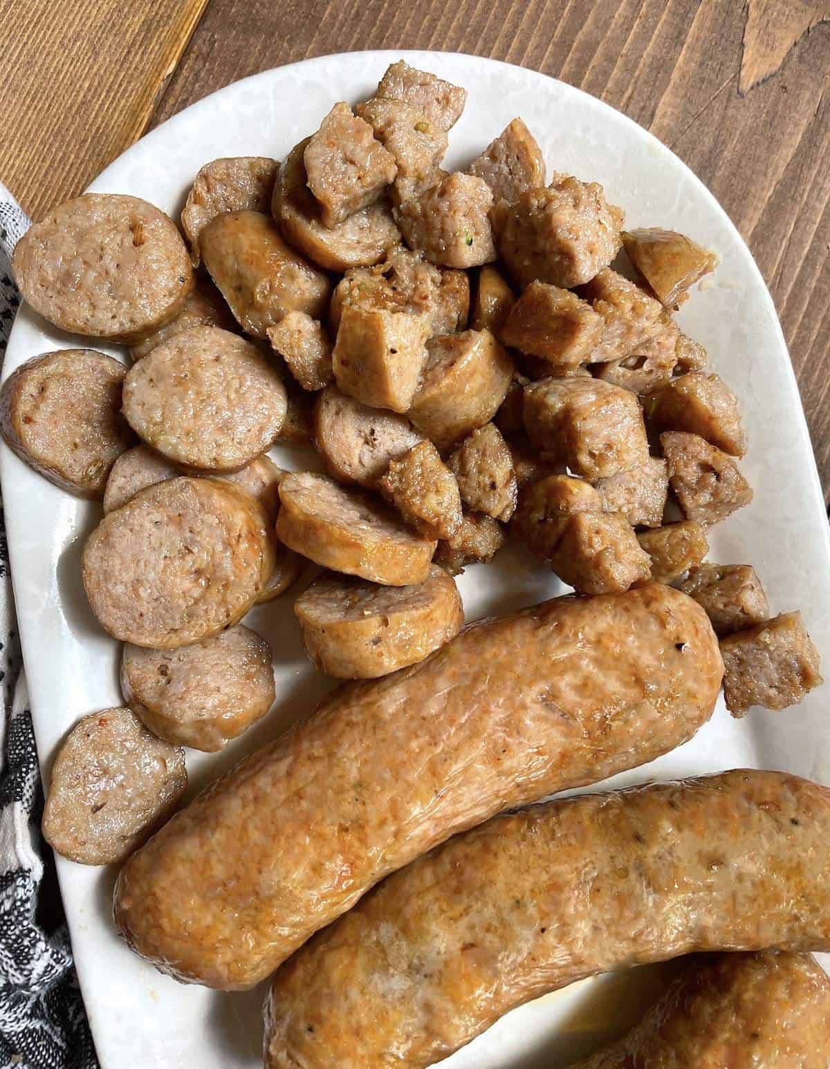 Air fried Italian sausage cut different ways on a white plate.