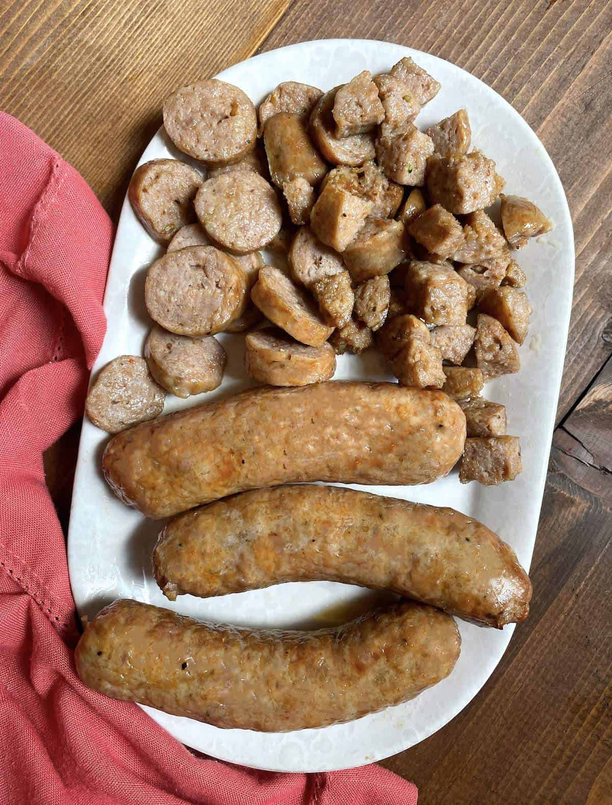 Air fried Italian sausages cut in different ways on a white plate with a pink napkin.