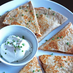 Sliced barbecue chicken quesadillas on a white plate with a small bowl of sour cream.