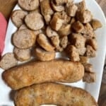 A white plate with cooked air fryer Italian sausage on it. Some whole and some cut.