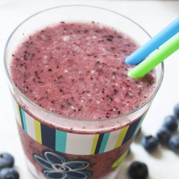 A blueberry banana peanut butter smoothie in a glass with two straws.