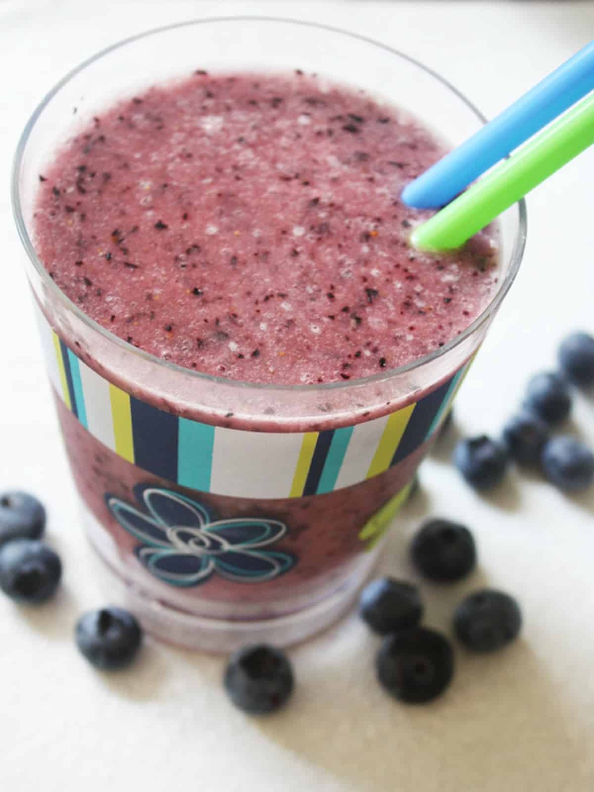 A banana blueberry peanut butter smoothie in a glass with two straws.