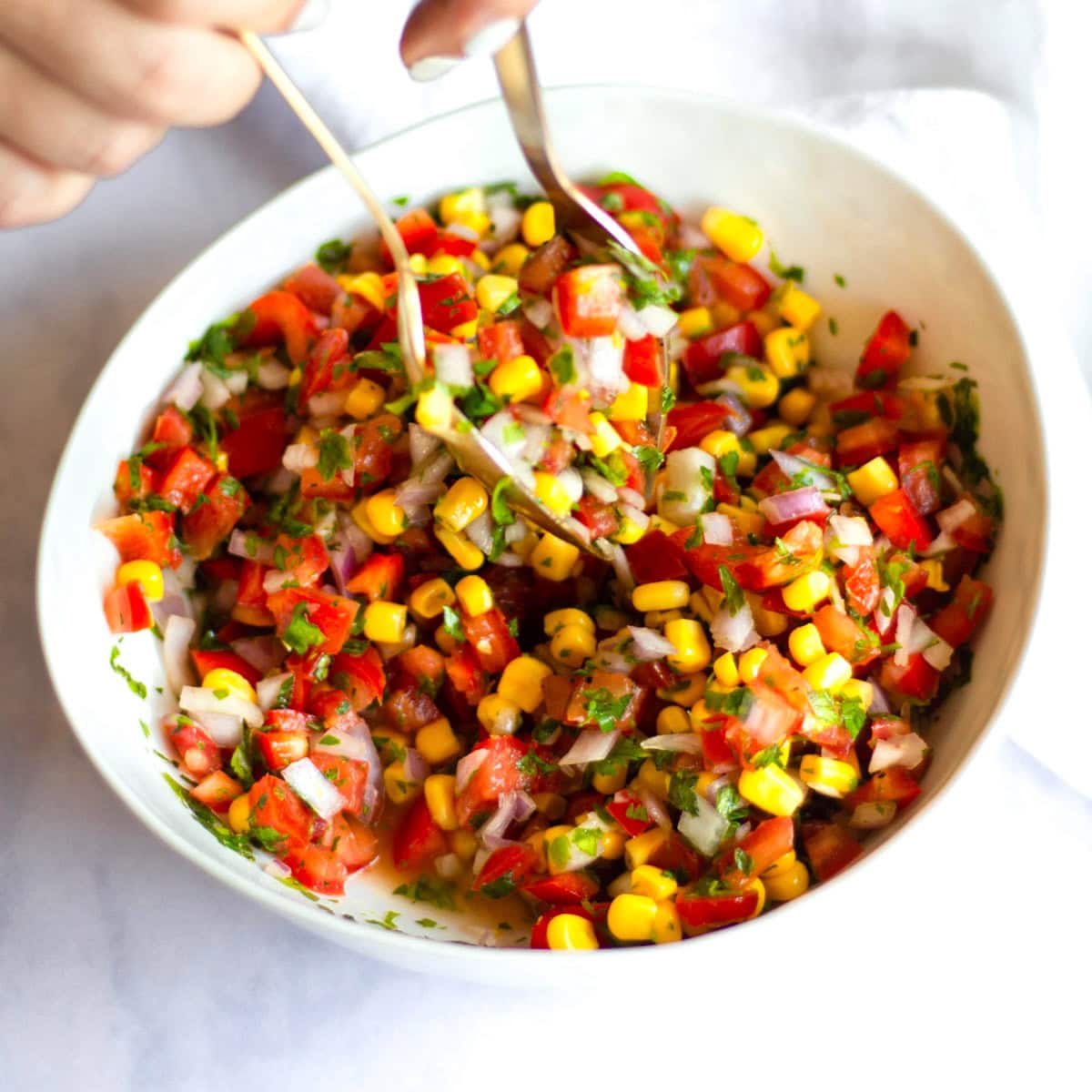 Two spoons tossing corn pico de gallo to mix it up.