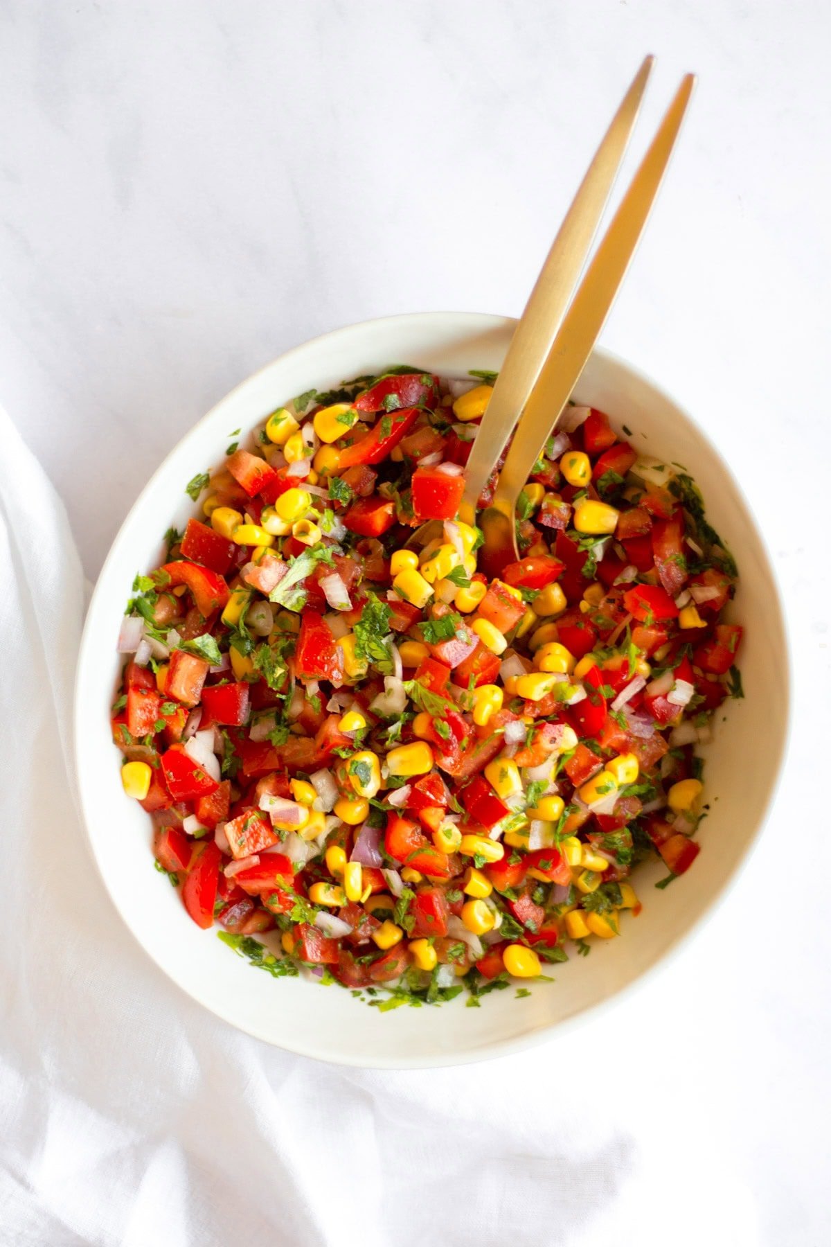A bowl of mixed corn salsa with two gold spoons in it.