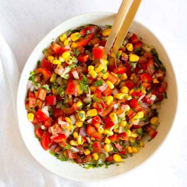 A bowl of mixed corn pico de gallo with two gold spoons.