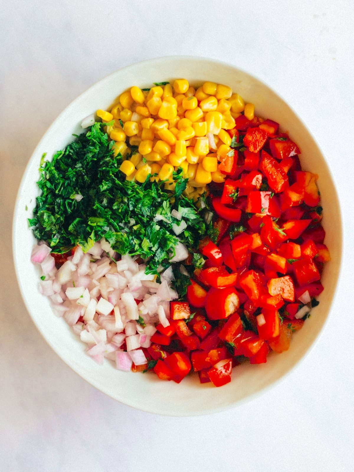 A bowl with the ingredients need to make corn salsa; diced peppers, red onion, corn, cilantro, and tomatoes.