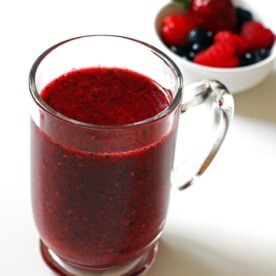 A mug of Triple Berry Smoothie with a bowl of mixed berries behind it.