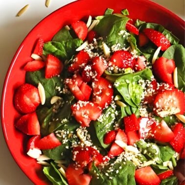 A red bowl with strawberry spinach salad with slivered almonds and poppyseed dressing.