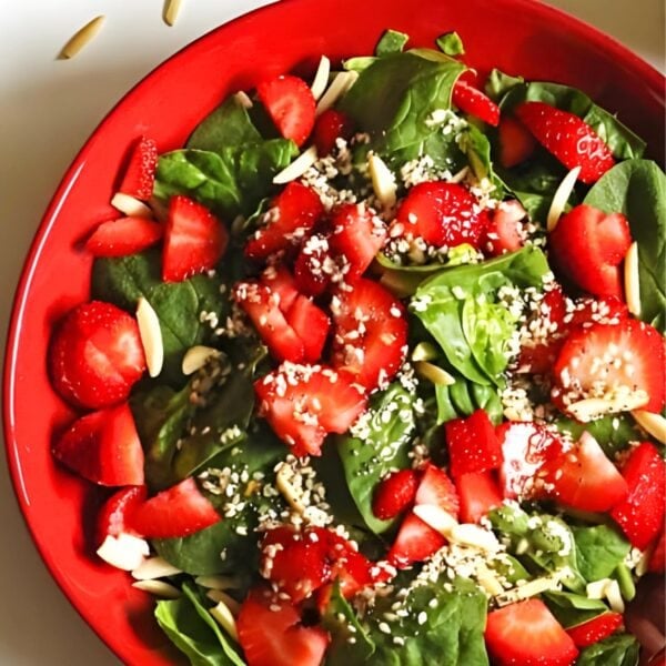 A red bowl with strawberry spinach salad with slivered almonds and poppyseed dressing.