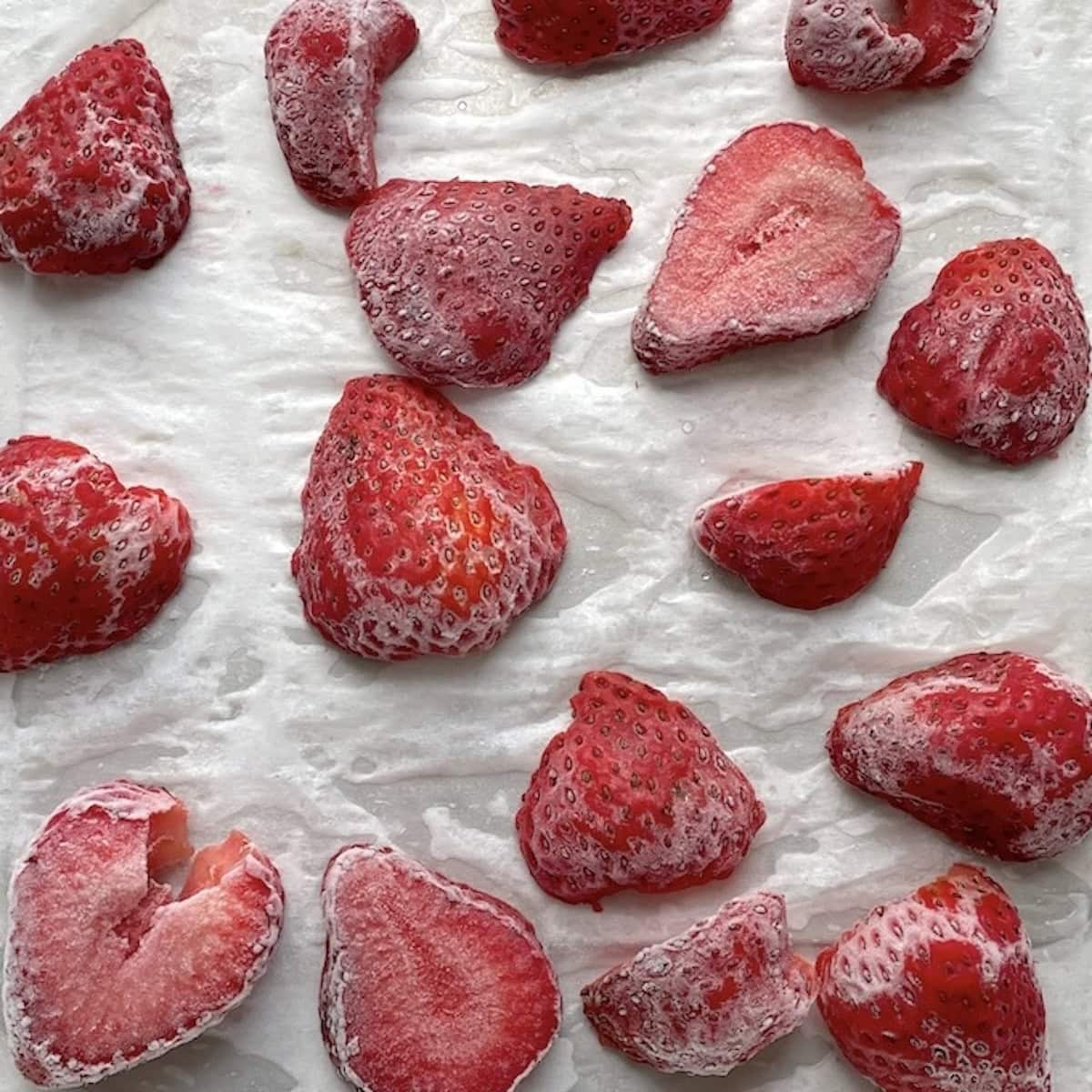 Thinly sliced frozen strawberries on a piece of parchment paper.