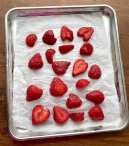 Sliced strawberries spread on a tray covered in parchment for freezing for smoothies.