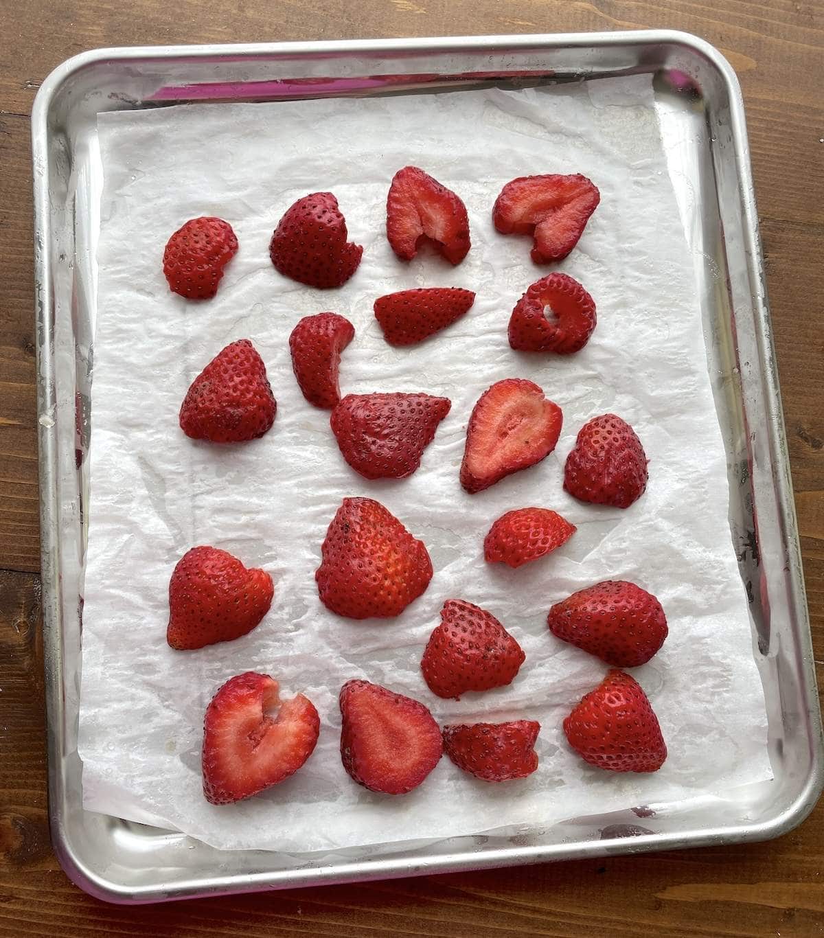 Sliced strawberries spread on a tray covered in parchment for freezing for smoothies.