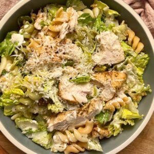 A blue bowl of chicken caesar pasta salad with rotini and a pink tea towel.
