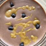 A chocolate peanut butter and banana smoothie with peanut butter drizzled over the top and chocolate chips sprinkled around.