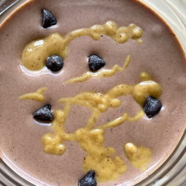 A chocolate peanut butter and banana smoothie with peanut butter drizzled over the top and chocolate chips sprinkled around.