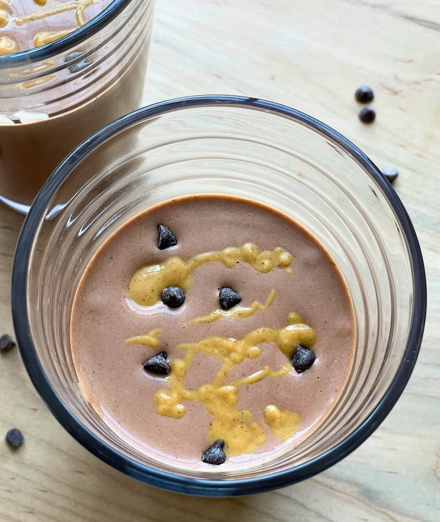 A chocolate peanut butter banana smoothie with peanut butter drizzled over the top and chocolate chips sprinkled around.