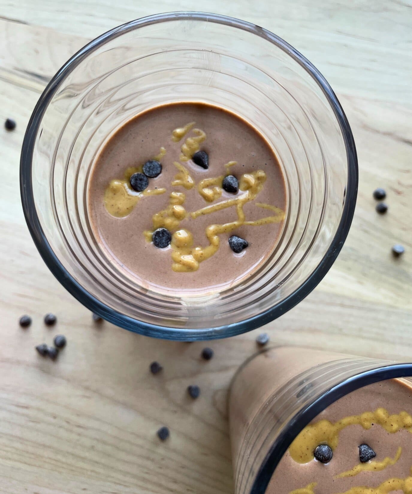 A chocolate peanut butter banana smoothie with peanut butter drizzled over the top and chocolate chips sprinkled around.