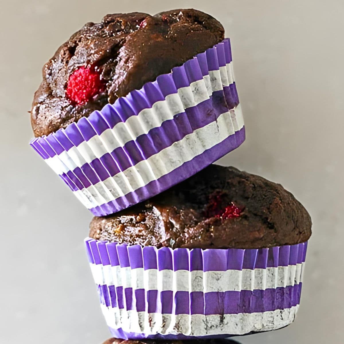 Two dark chocolate raspberry banana muffins stacked on top of each other.