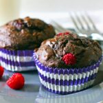 Two dark chocolate raspberry banana muffins on a blue plate.
