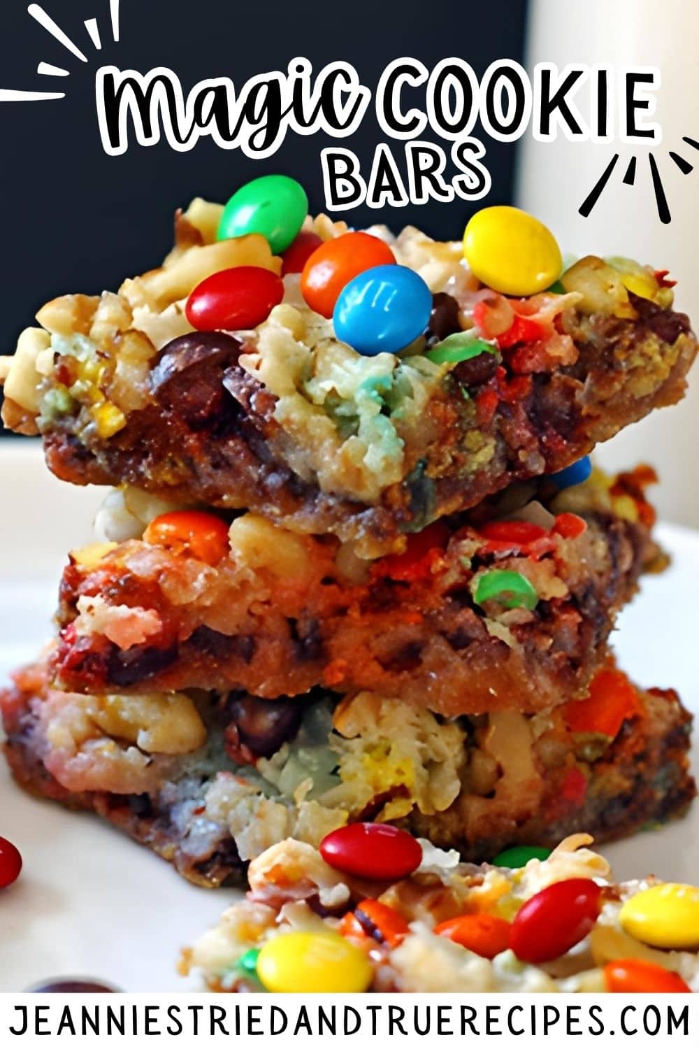 A pin image of four magic cookie bars with nuts, coconut, chocolate chips, and mini m and ms stacked on a white plate with a glass of milk.