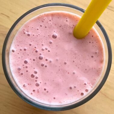 A close-up of a strawberry banana smoothie with Greek yogurt with a yellow straw.