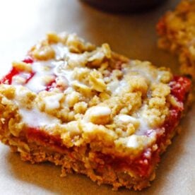 A glazed strawberry rhubarb crumble bar on a tray covered in brown parchment paper.
