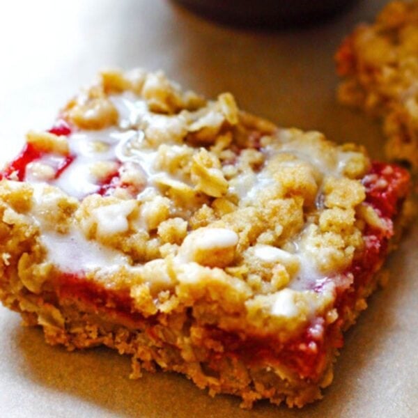 A glazed strawberry rhubarb crumble bar on a tray covered in brown parchment paper.