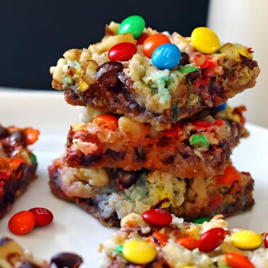 Gooey magic cookie bars with nuts, coconut, chocolate chips, and mini m and ms stacked on a white plate with a glass of milk.